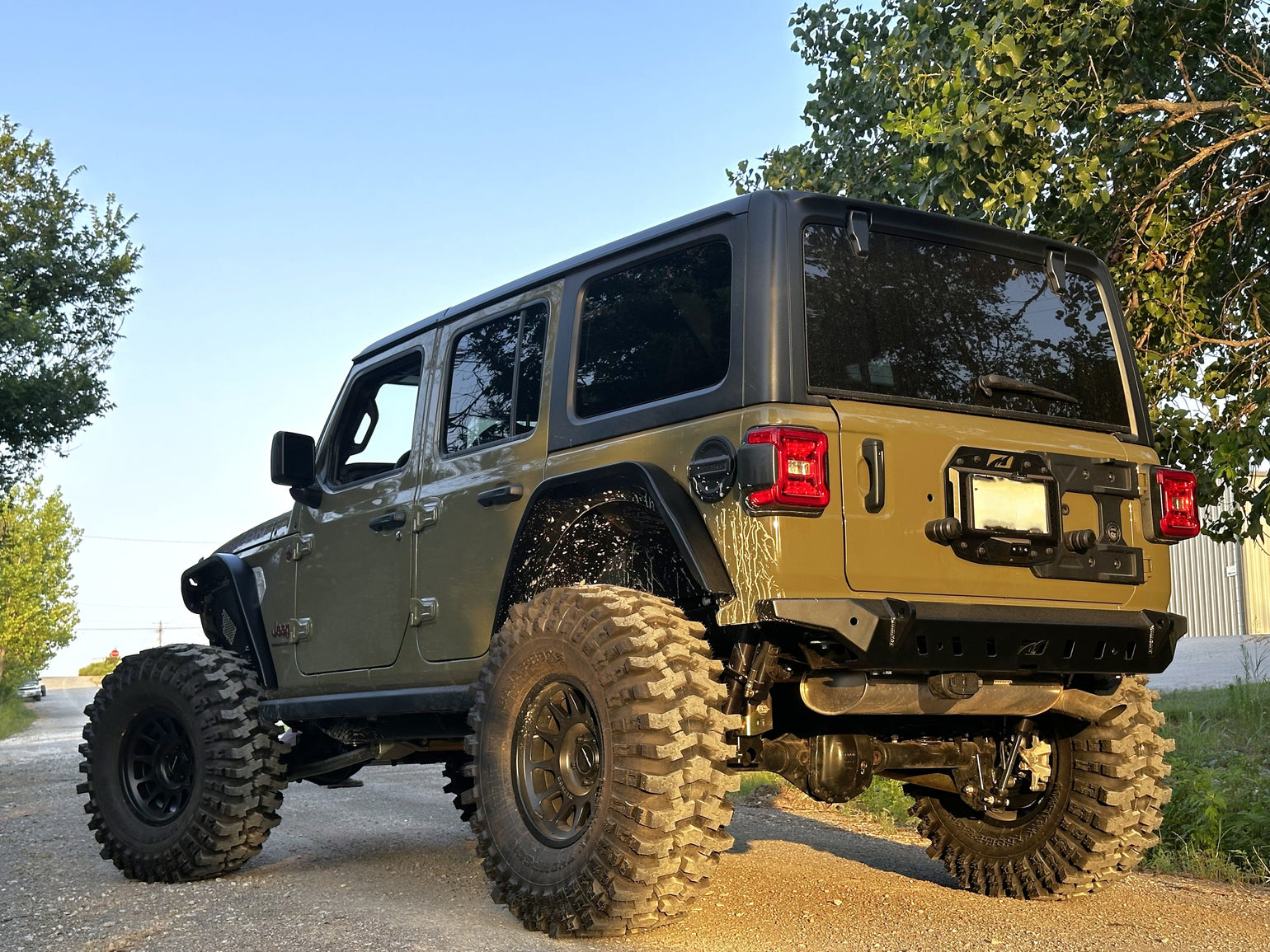 Green Jeep Wrangler with large off-road tires on a road with trees in the background
